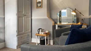 A room with a grey sofa, a white wardrobe, a small table with a kettle, and a mirror on a wooden stand. - Goodwin House (Keswick)