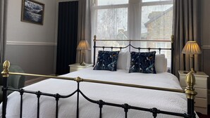 A neatly made bed with a white duvet, two bedside tables with lamps, a large window with curtains, and a framed picture on the wall. - Goodwin House (Keswick)