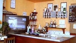 Un espace bar équipé d’un téléviseur, d’étagères remplies de bouteilles et d’un tableau affichant le menu.