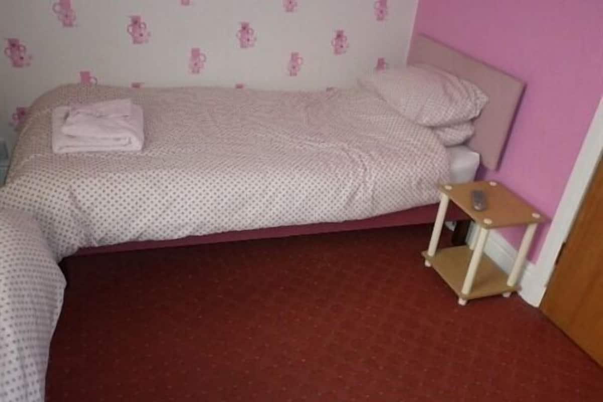 Una cama individual con cabecera rosa y una mesita de noche pequeña.