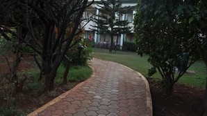 A paved pathway curving through a landscaped area with trees and a building in the background. - Blue Country Resort (Mahabaleshwar)