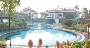 A swimming pool with a bridge, surrounded by greenery and buildings.