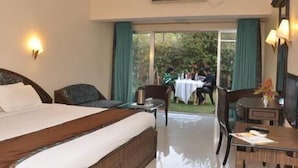 A hotel room with a large bed, a small table, a chair, and a view of an outdoor area with people. - Blue Country Resort (Mahabaleshwar)