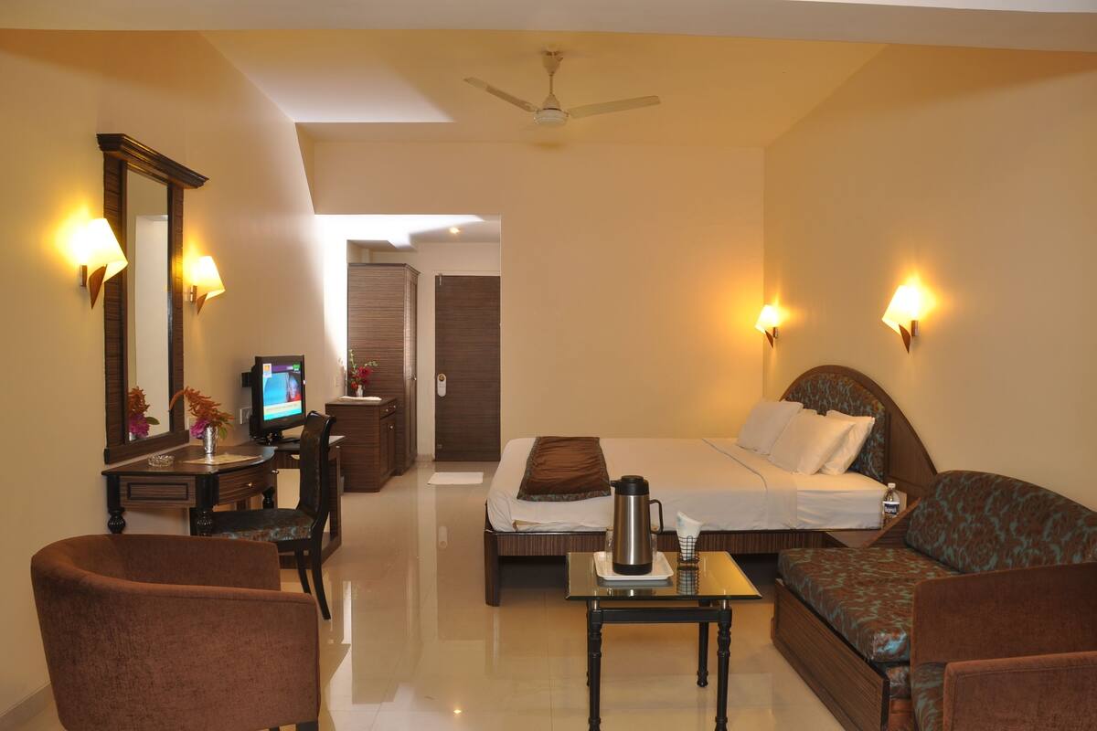 A hotel room with a bed, sofa, desk, and a television.