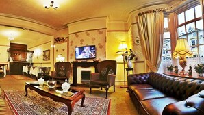 A spacious living room with a leather sofa, a fireplace, and a television. - Wilsons Hotel - Blackpool Tower View (Blackpool)