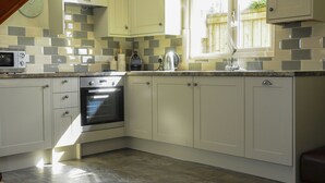 A kitchen with white cabinets, a built-in oven, a microwave, and a window with a view of the outside. - The Poplars (Thirsk)