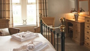 A hotel room with a bed, a wooden dresser, a chair, and a window with curtains. - The Poplars (Thirsk)
