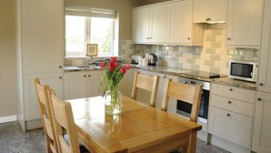 A kitchen with white cabinets, a wooden dining table, and a vase with flowers. - The Poplars (Thirsk)