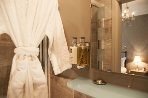 A bathroom with a robe hanging, a glass sink, and toiletries on the wall.