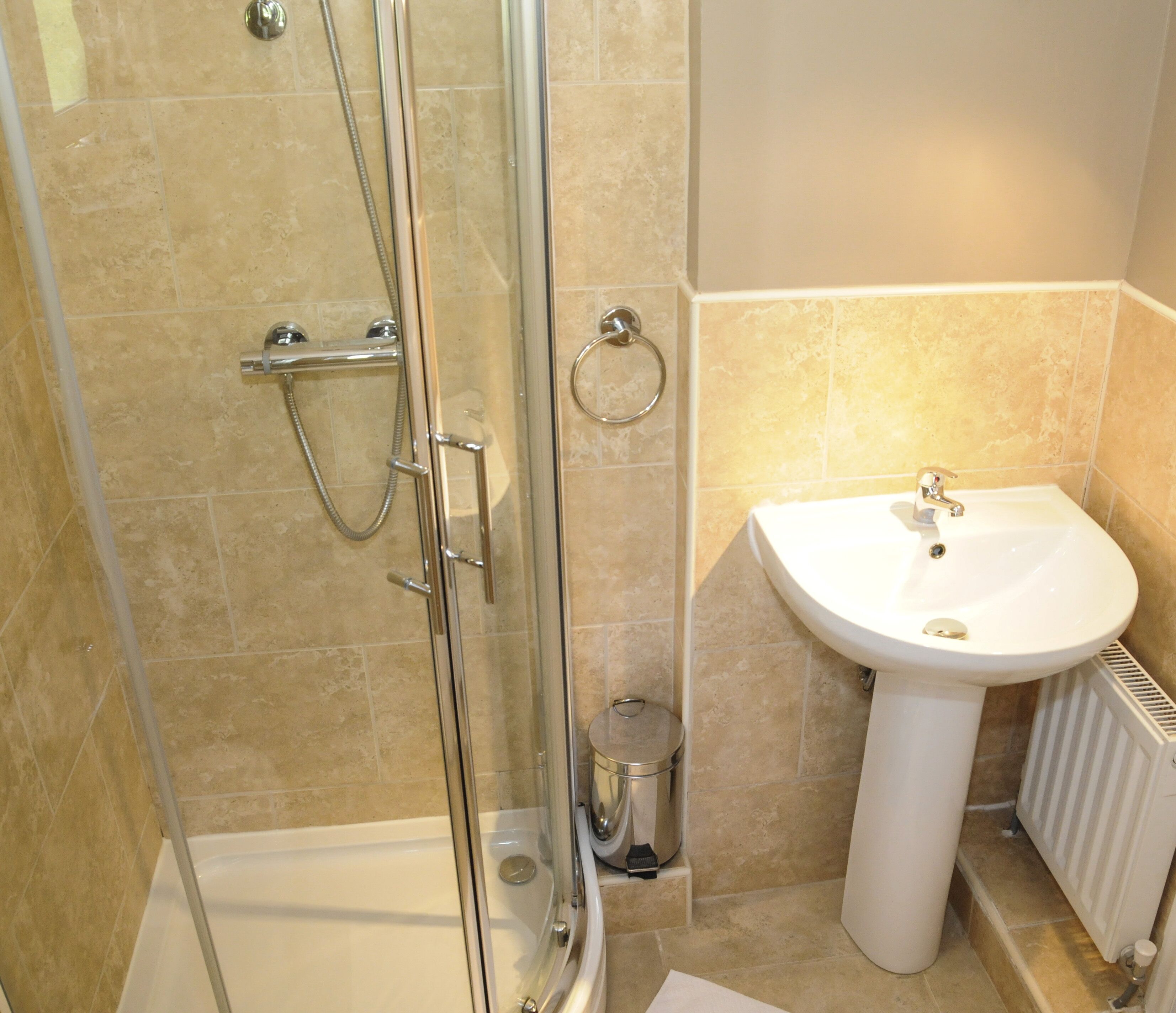 Une salle de bain avec une douche à parois de verre, un lavabo blanc et un radiateur.