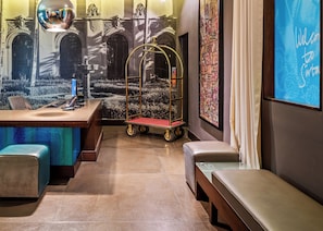 A modern hotel lobby with a reception desk, seating area, and a mural of a cityscape. - SIRTAJ - Beverly Hills (Beverly Hills)