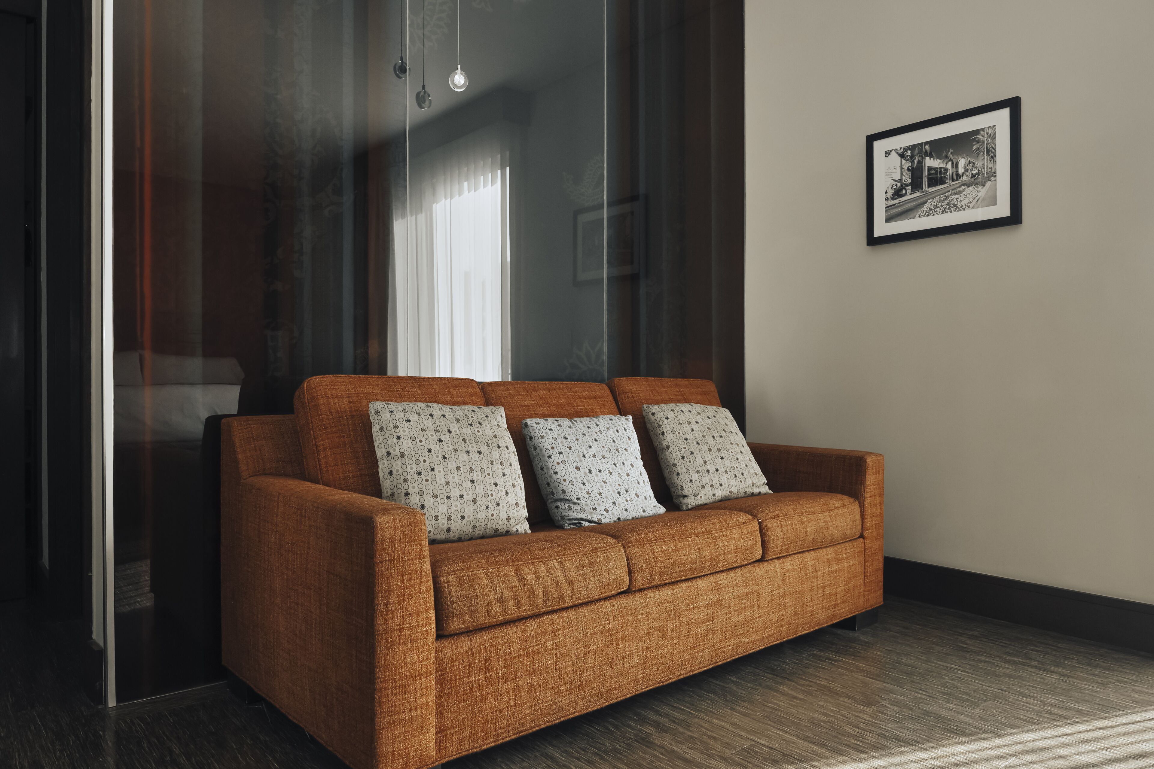 Un salon moderne avec un canapé marron, des coussins à motifs, un tableau encadré au mur et une cloison en verre.