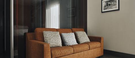 Un salon moderne avec un canapé marron, des coussins à motifs, un tableau encadré au mur et une cloison en verre.