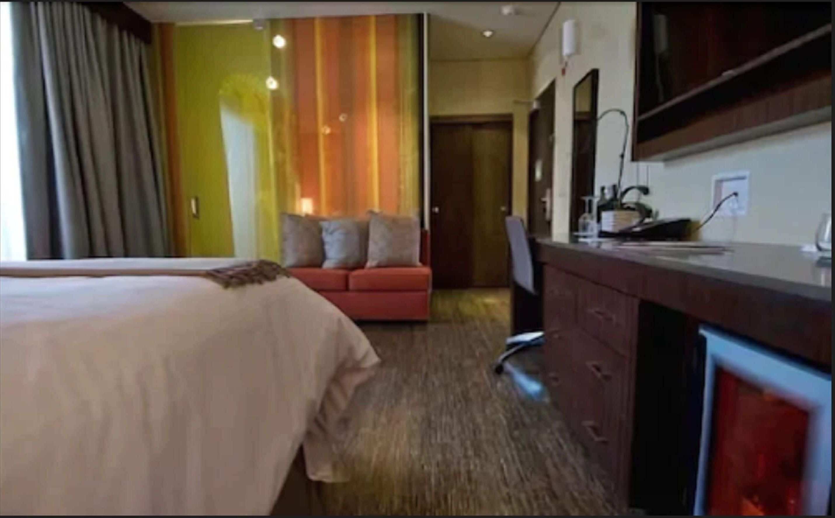 A hotel room with a bed, a desk, a red sofa, and a mirror.