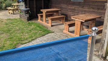 A wooden outdoor seating area with picnic tables and a blue safety net.