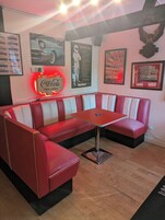 A retro-themed seating area with a neon sign, vintage posters, and a wooden signboard.