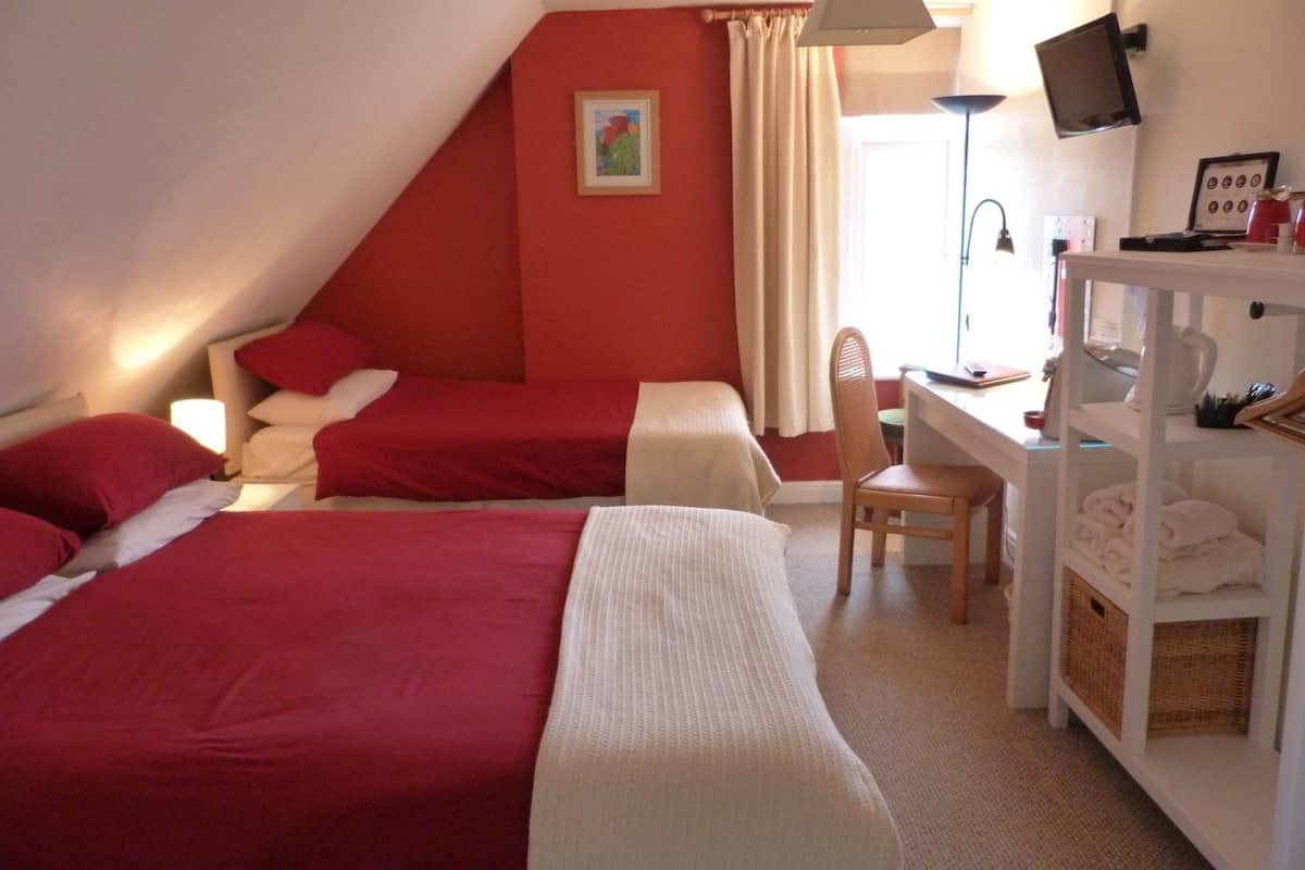 A hotel room with two beds, a desk, a chair, a TV, and a shelf with towels.