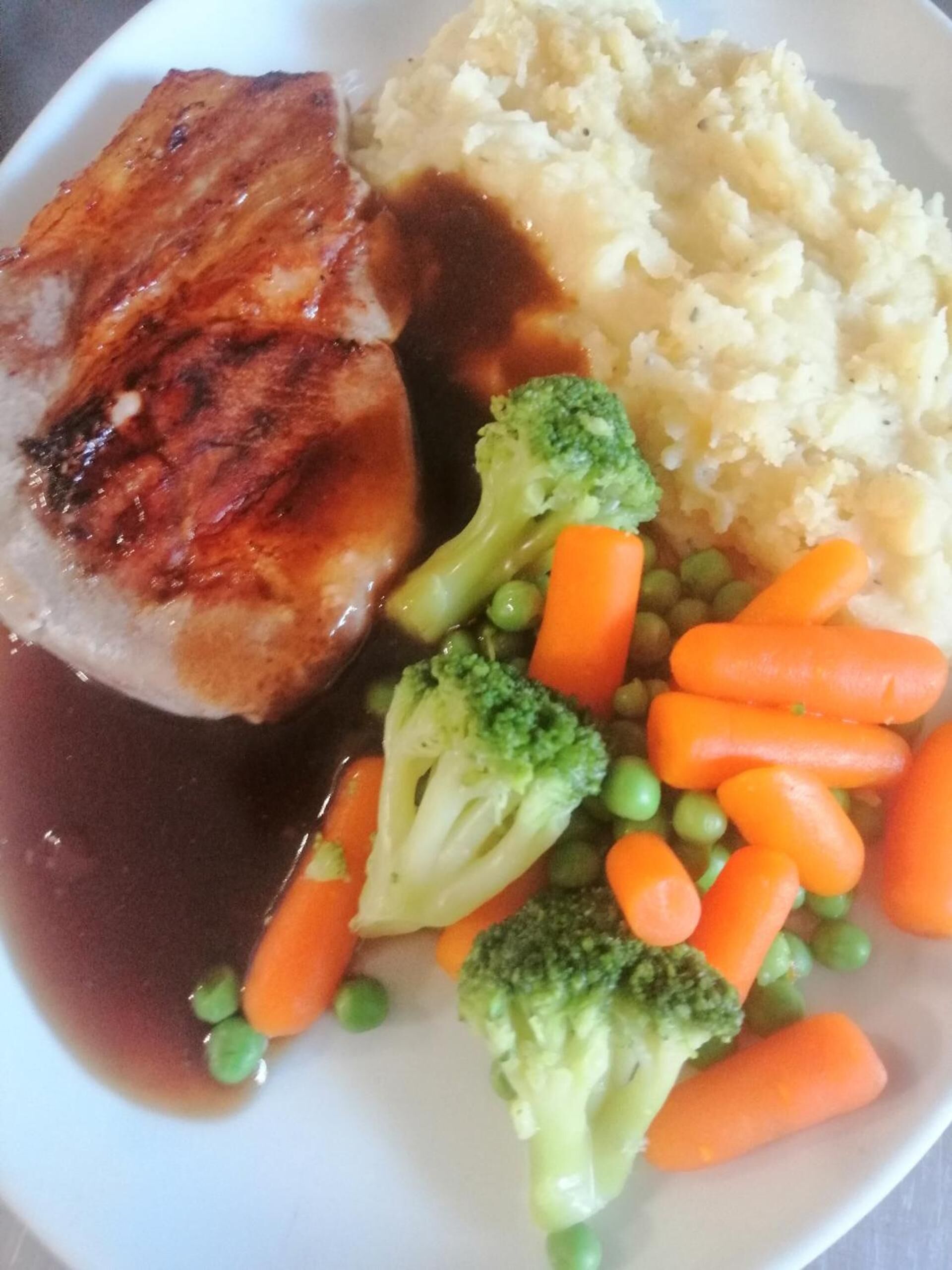 Un plato con carne, puré de papas y verduras al vapor, incluyendo brócoli y zanahorias.
