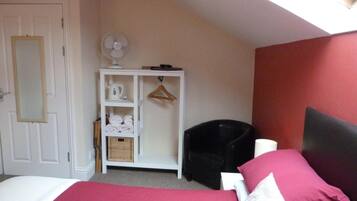 A bedroom with a bed, a white wardrobe, a black chair, a fan, and a red wall.