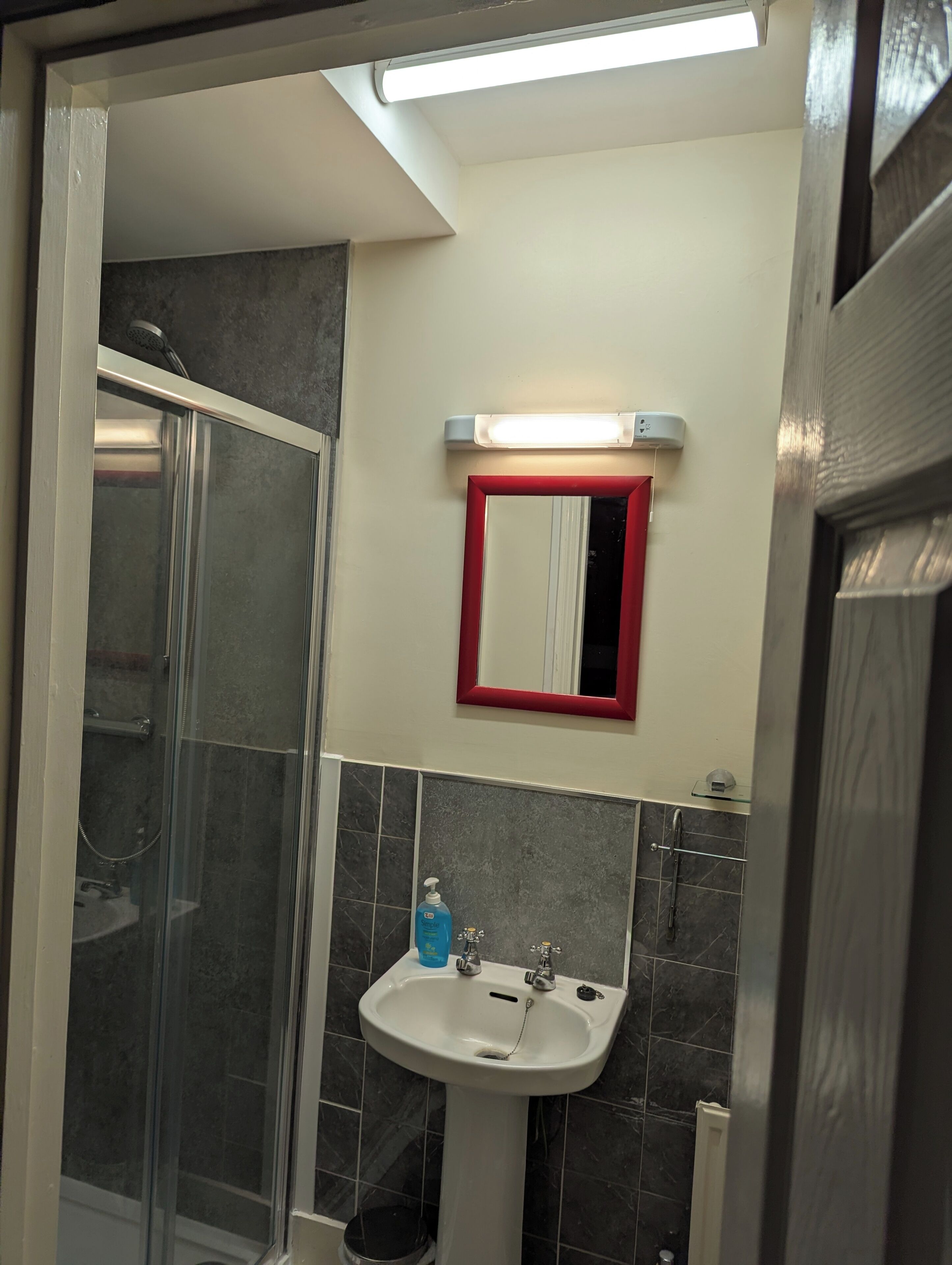 Un baño con cabina de ducha de vidrio, un lavabo blanco con un espejo encima y un espejo con marco rojo.