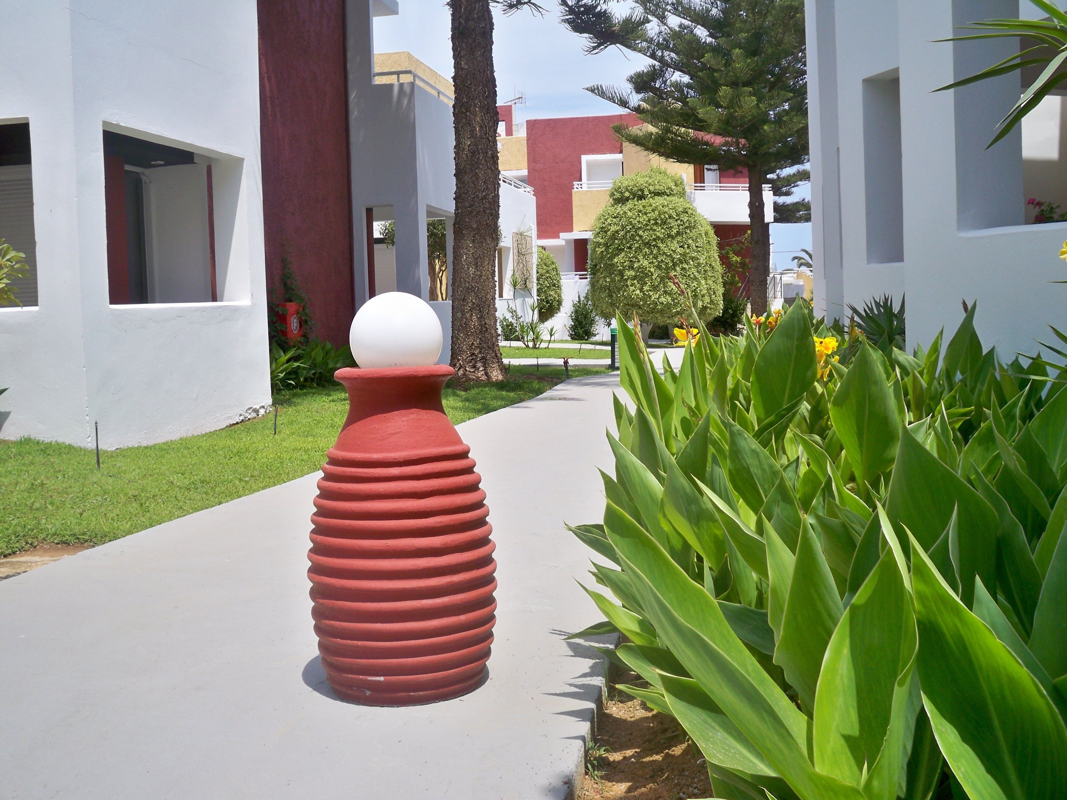 A pathway lined with green plants and a red sculpture.