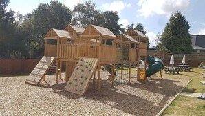 A wooden play structure with multiple climbing areas and a slide. - The Star Inn (Lingfield)