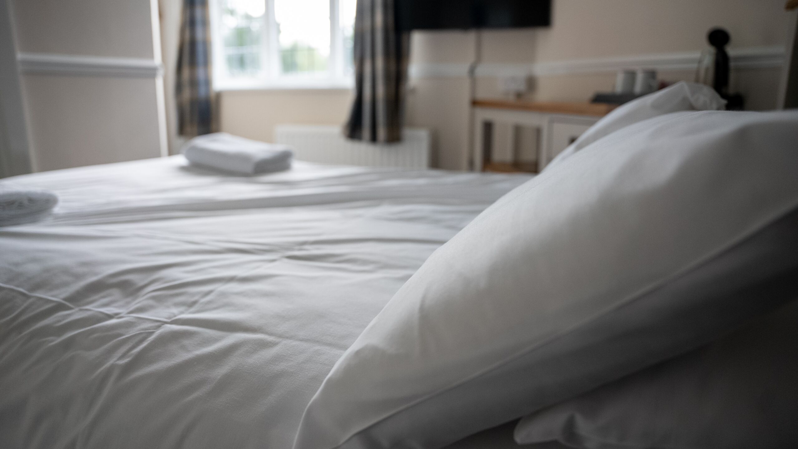 Una cama bien hecha con sábanas y almohadas blancas en una habitación con ventana y radiador.