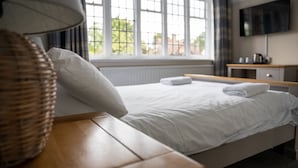 A neatly made bed with white linens and a pillow, a wooden bedside table with a lamp, and a TV mounted on the wall. - The Star Inn (Lingfield)