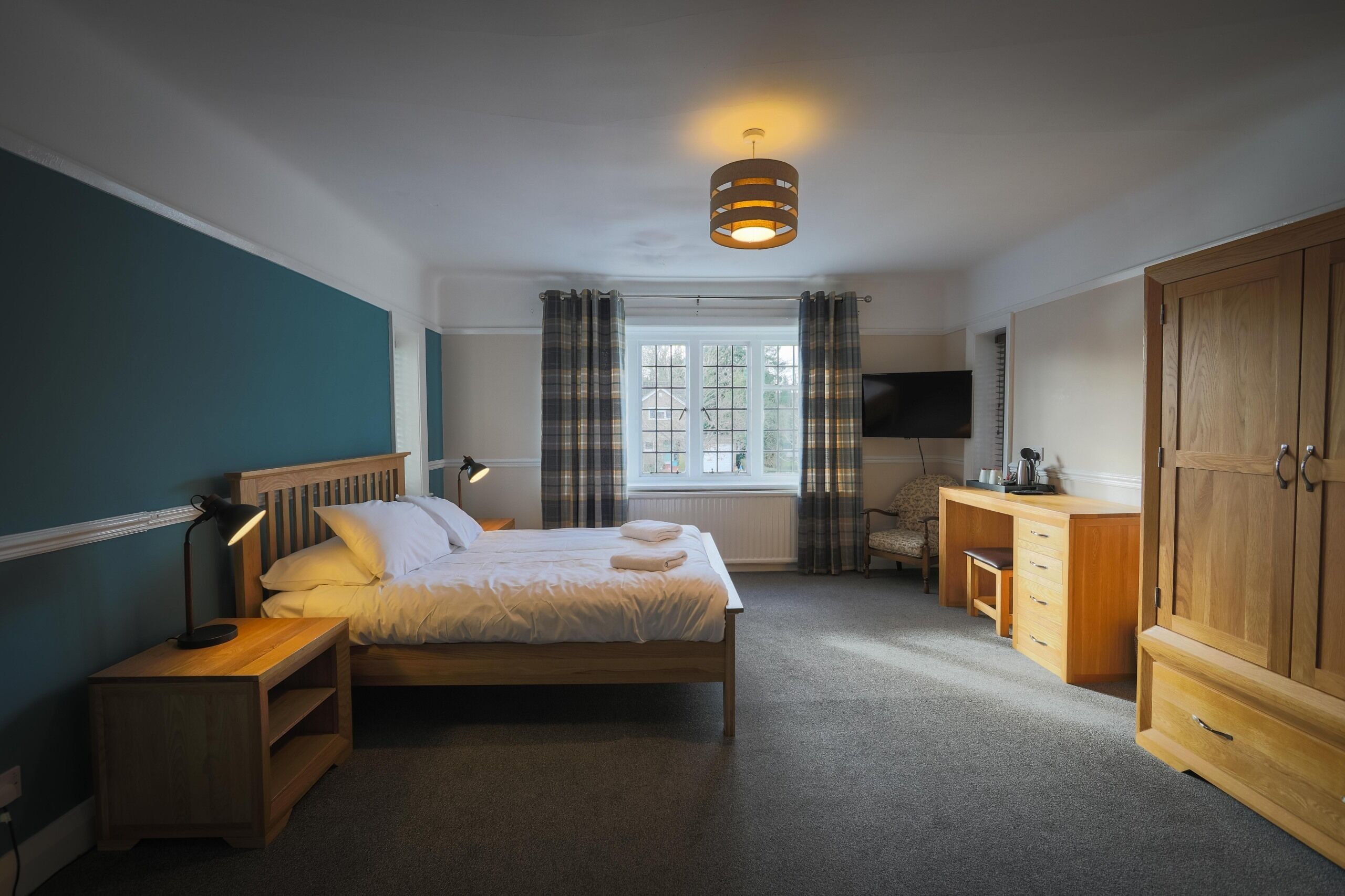 A bedroom with a bed, bedside table, lamp, wooden wardrobe, and a television.