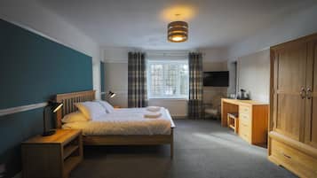 A bedroom with a bed, bedside table, lamp, wooden wardrobe, and a television.
