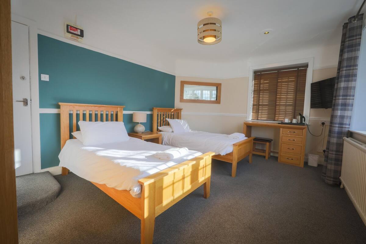 A bedroom with two wooden beds, a desk, a chair, a radiator, and a window with blinds.