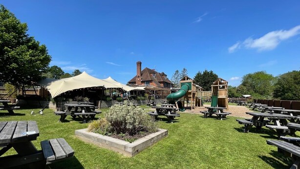 A park with picnic tables, a playground, and a building with a chimney. - The Star Inn (Lingfield)