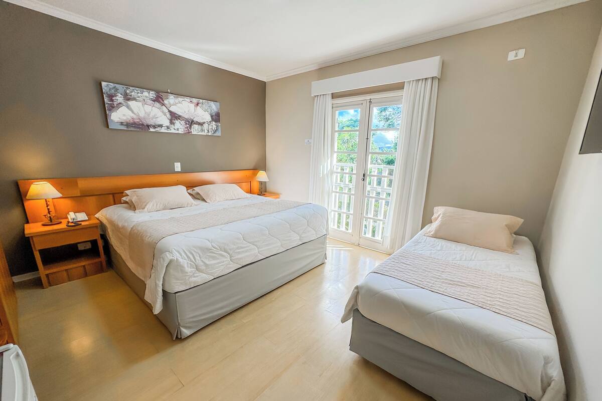 Une chambre d’hôtel avec deux lits, une table de chevet avec une lampe, un tableau au mur et une fenêtre avec des rideaux.