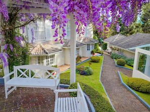 Een tuin met een witte bank, een pad en een huis met pannendak.