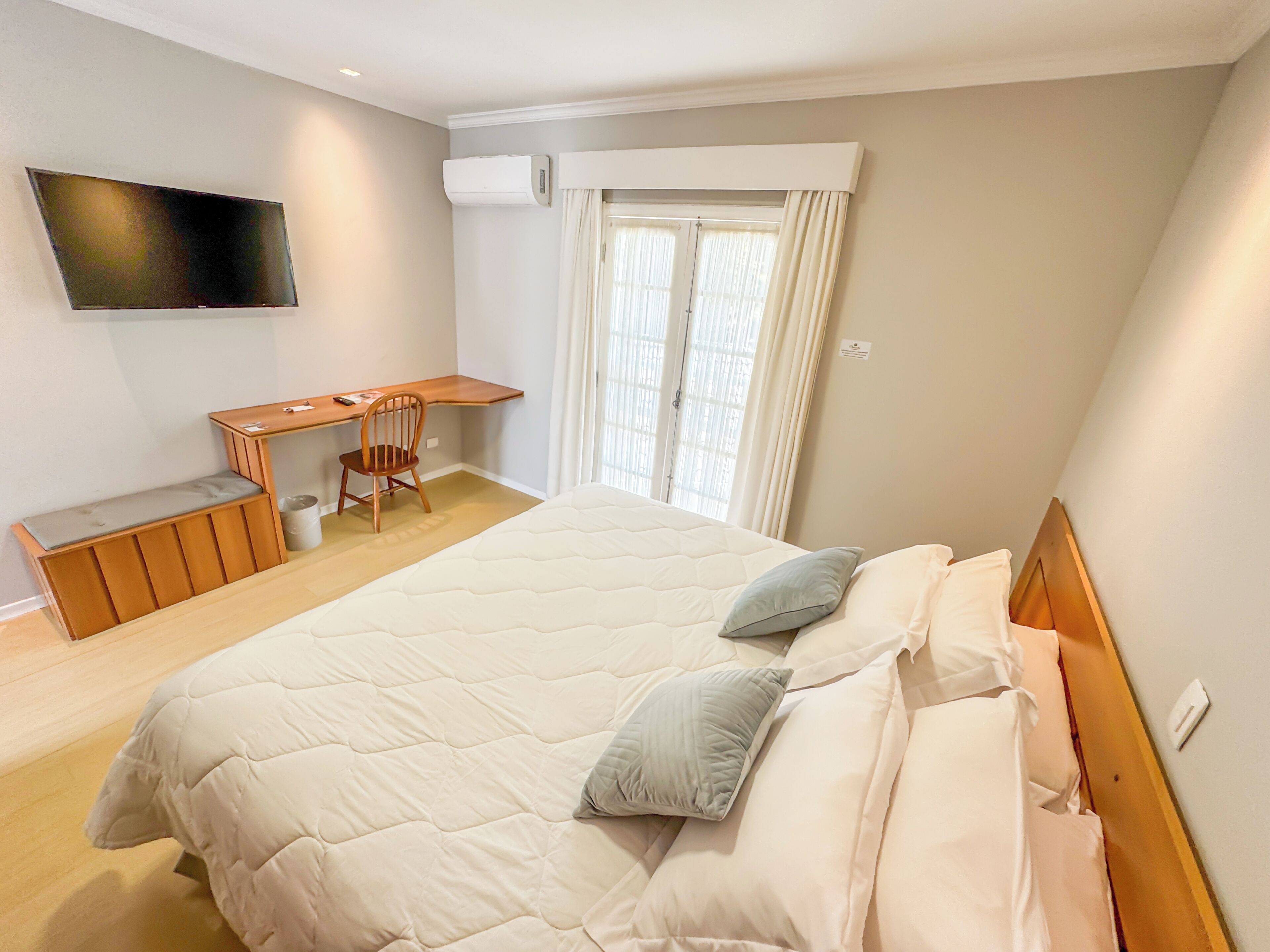 A bedroom with a large bed, a desk, a chair, and a TV mounted on the wall.