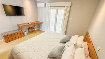 A bedroom with a large bed, a desk, a chair, and a TV mounted on the wall.