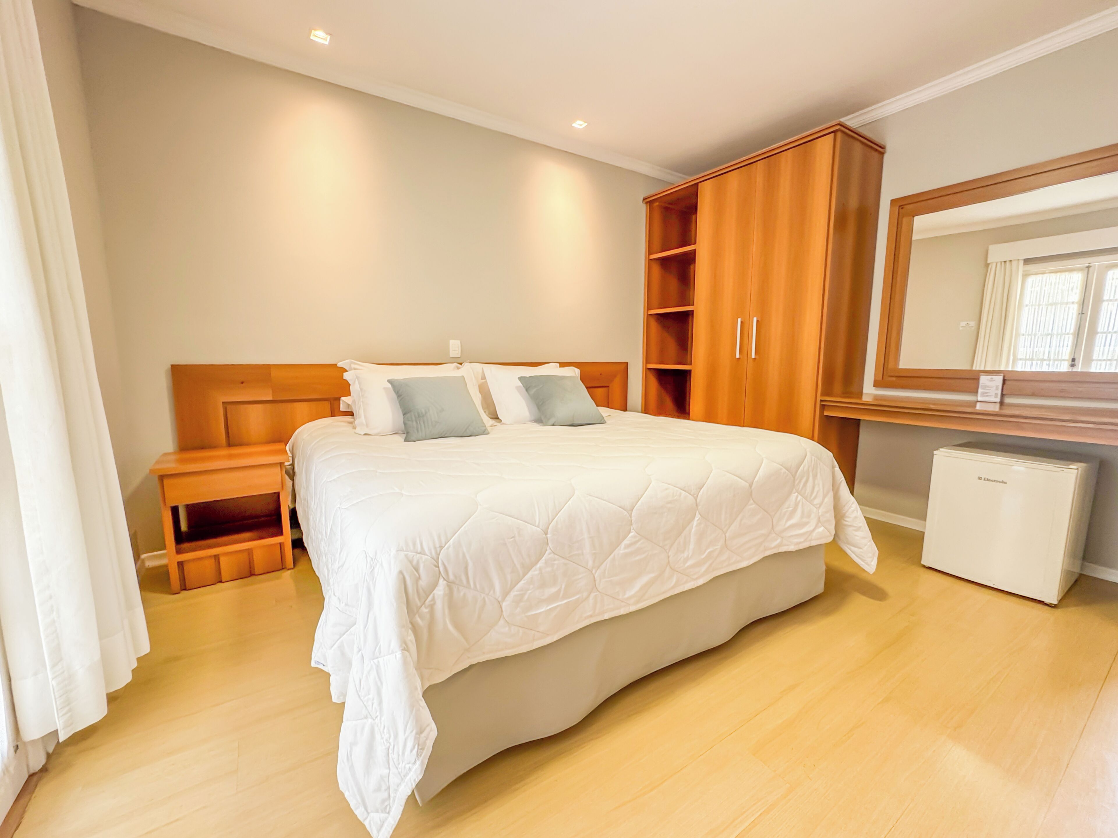 A bedroom with a bed, wooden wardrobe, bedside tables, and a small refrigerator.