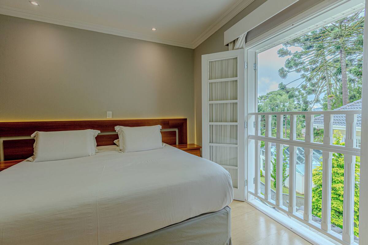 Une chambre avec un grand lit, une tête de lit en bois, une porte blanche et une vue sur la verdure.