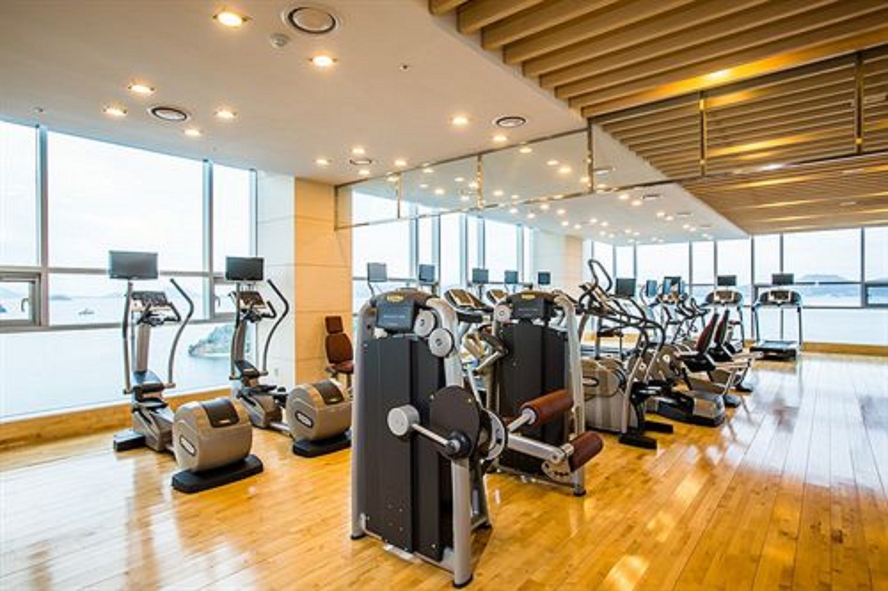 Ein Fitnessstudio mit verschiedenen Trainingsgeräten, großen Fenstern und Holzböden.