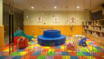 Zona de juegos infantiles con tapetes de colores, un tobogán y una estructura de juego circular.
