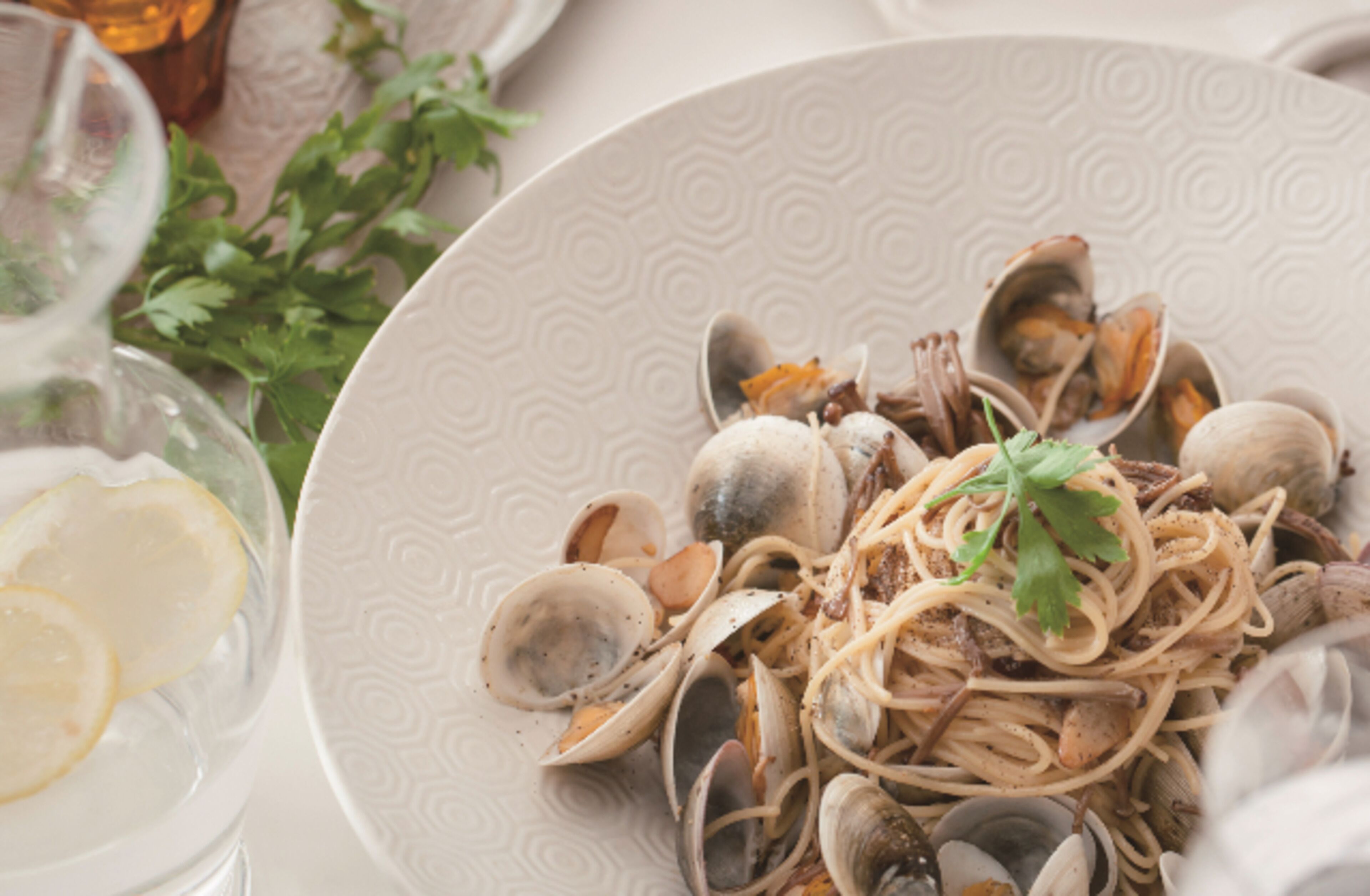 Ein Teller mit Muscheln, Pasta und einer Garnitur, dazu ein Glas Wasser und Zitronenscheiben.
