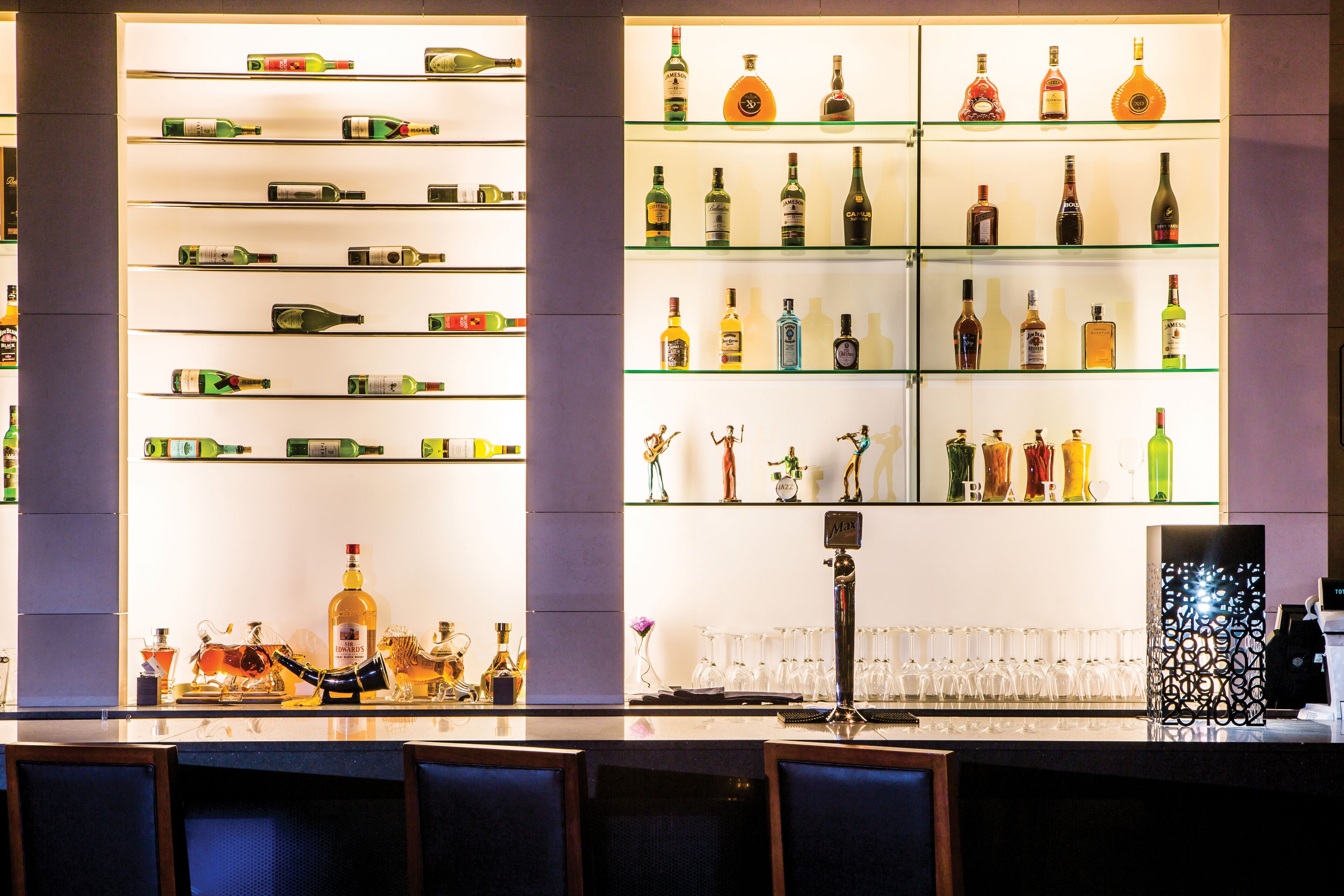 A bar area with shelves of various liquor bottles, a bar counter, and seating.