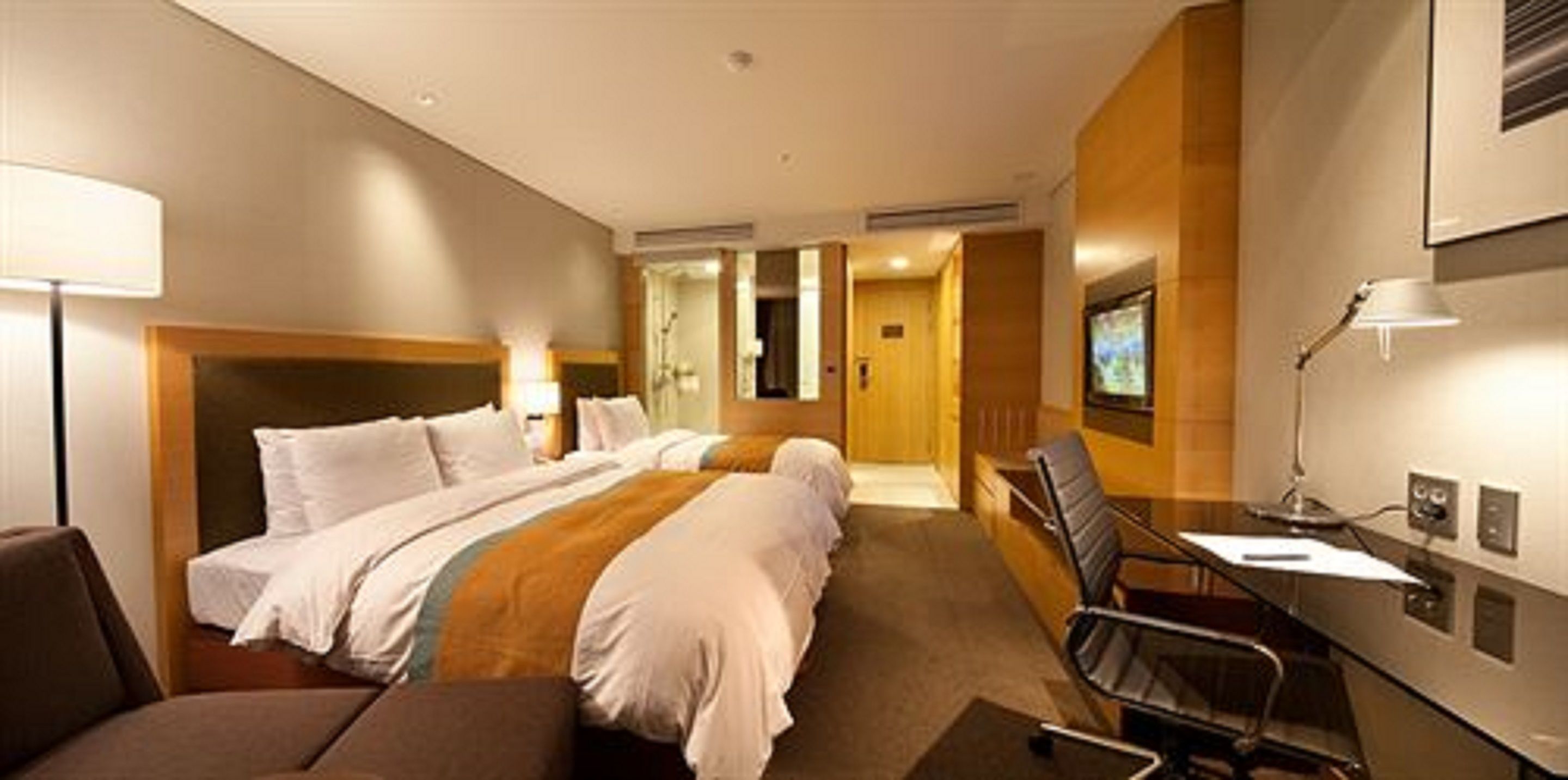Una habitación de hotel con una cama grande, un escritorio, una silla y un televisor montado en la pared.