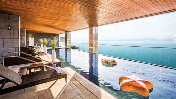 Ein Infinity-Pool mit Blick auf das Meer, einer Holzzieldecke und Liegestühlen.