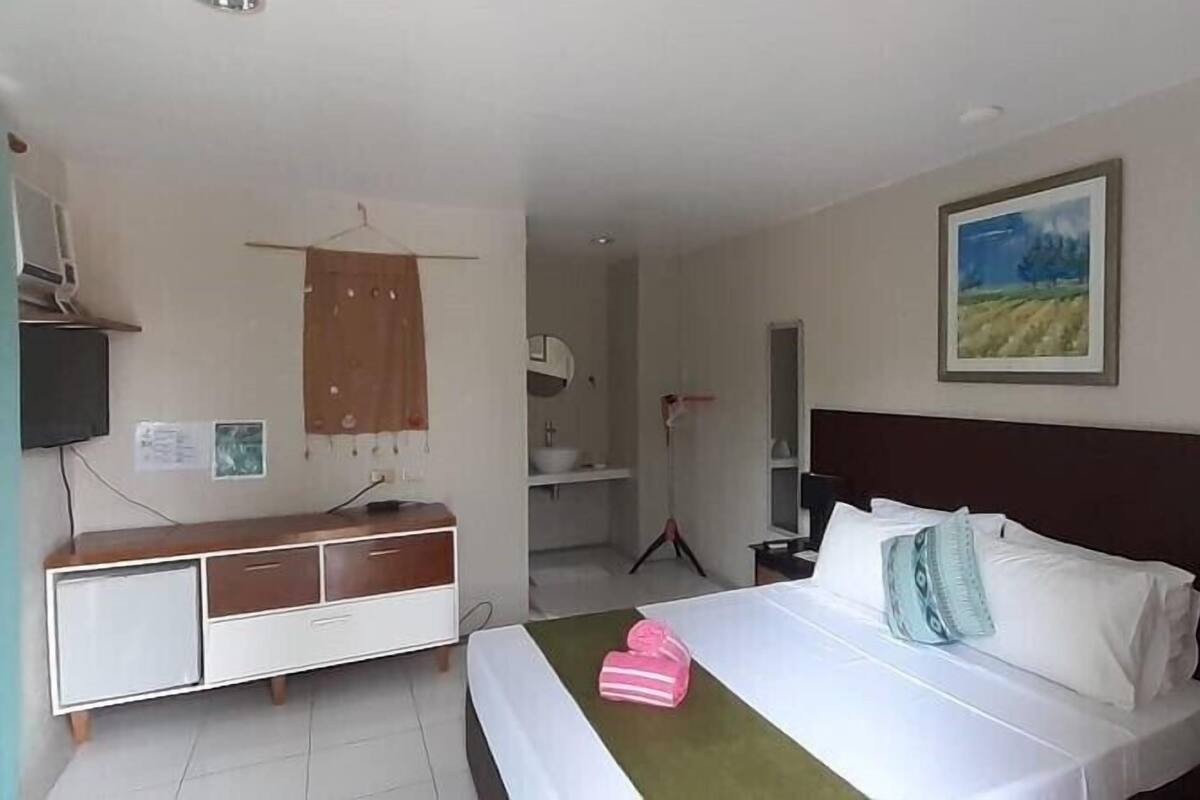 Ein Hotelzimmer mit einem Bett, einem Schminktisch, einem Spiegel, einem Gemälde und einem im Hintergrund sichtbaren Badezimmer.