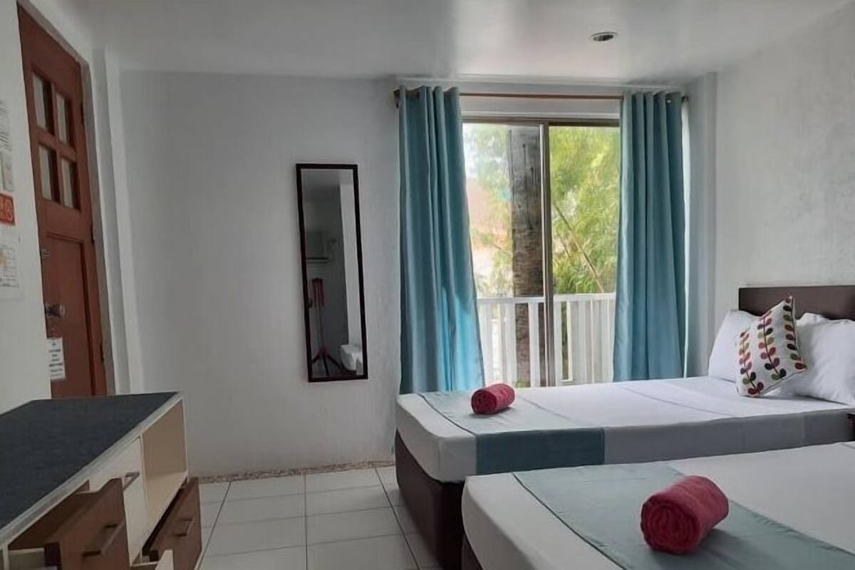 Ein Hotelzimmer mit zwei Betten, einem Schreibtisch, einem Spiegel und einem Fenster mit Vorhängen.