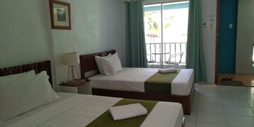 Habitación de hotel con dos camas, una mesita de noche con lámpara, un cuadro en la pared y un balcón con sillas.