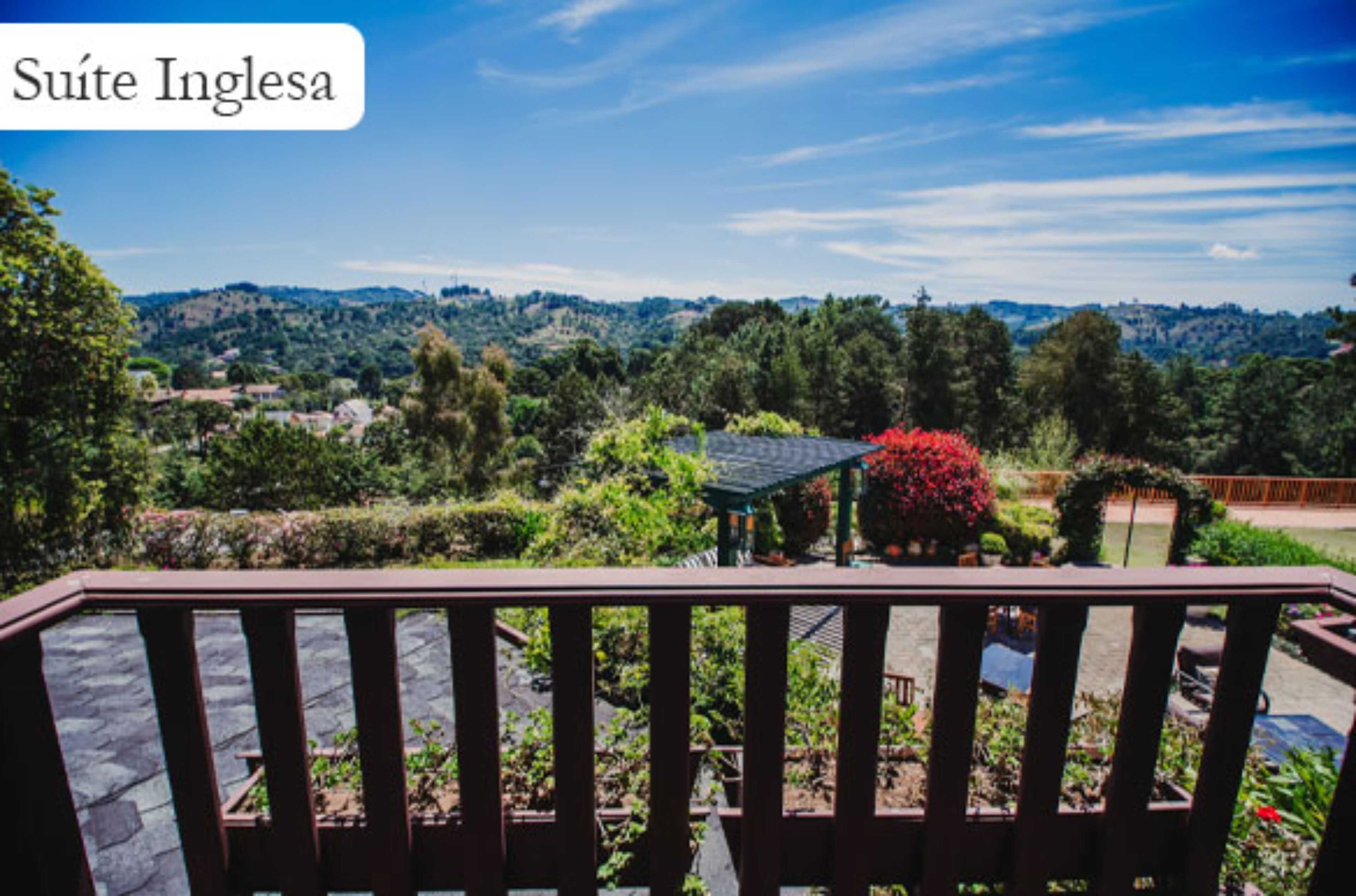 A view from a balcony with a wooden railing, overlooking a landscaped garden with a gazebo and red flowers.
