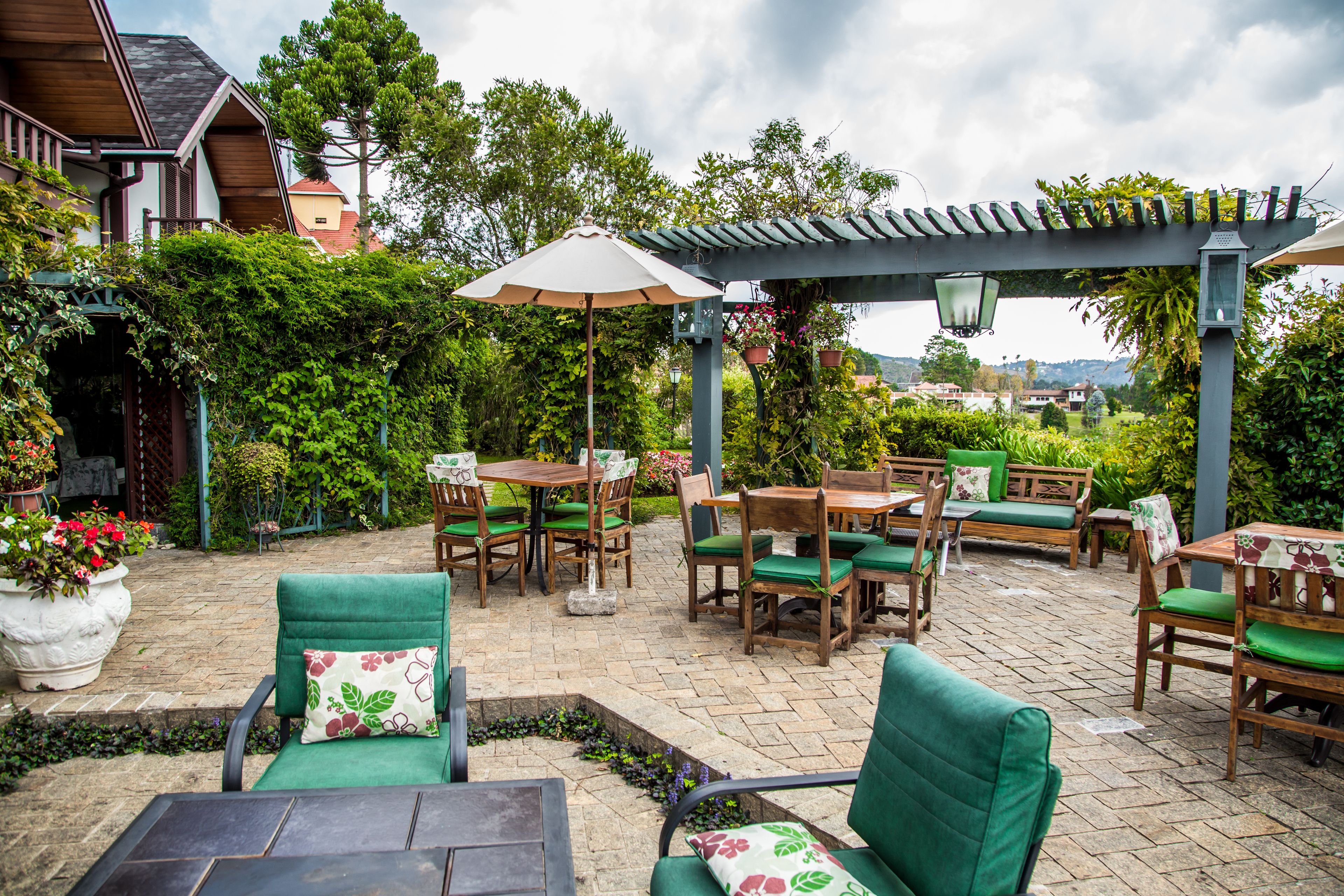 An outdoor patio with wooden furniture, green cushions, and potted plants.