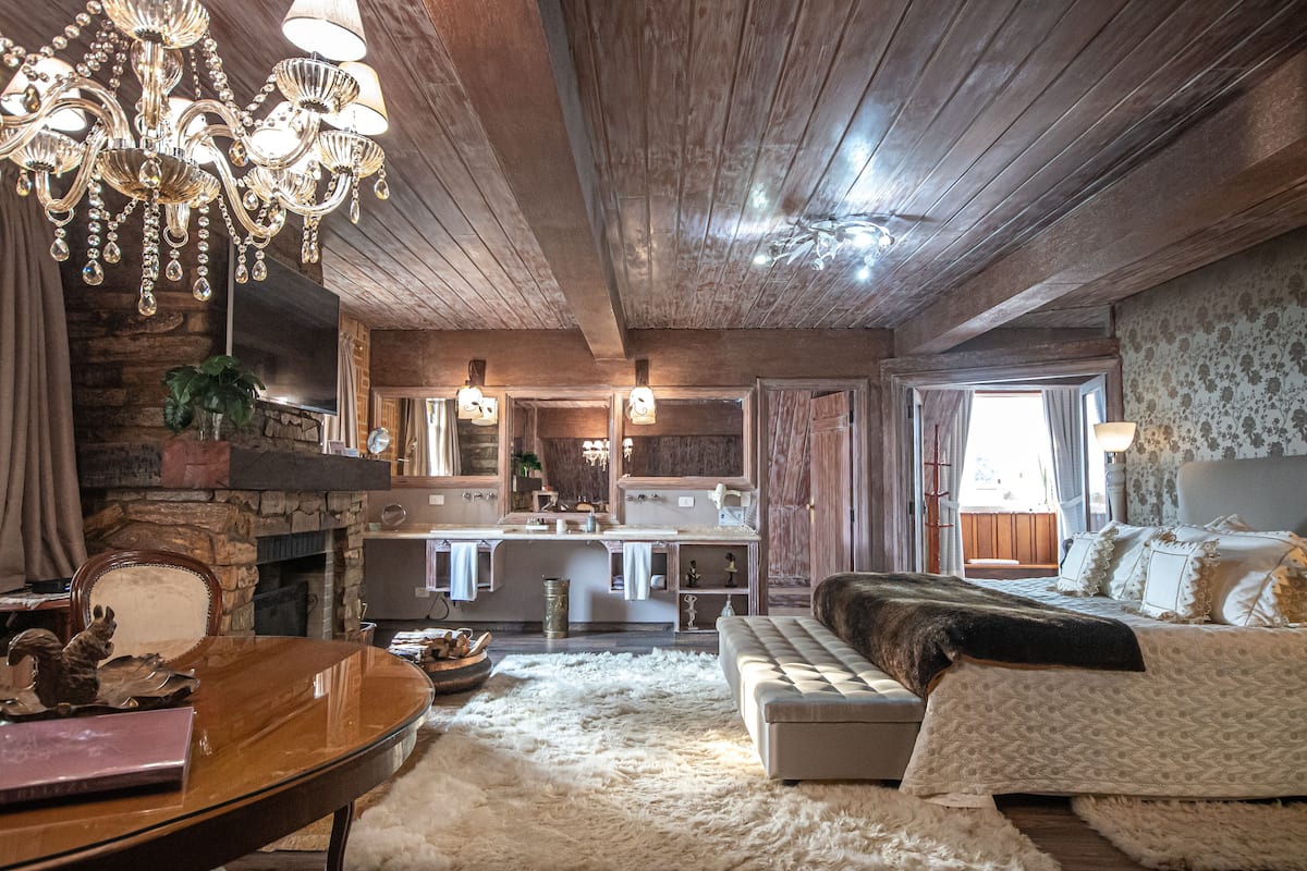 Un intérieur rustique agrémenté d’un lustre, d’un plafond en bois, d’une cheminée, d’un canapé et d’une table à manger.